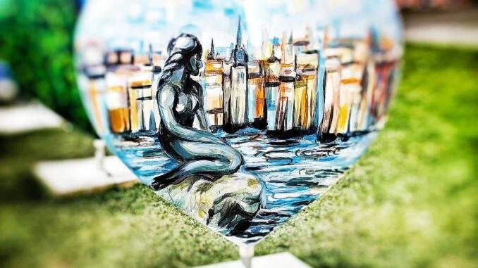 Vista alternativa de la Sirenita mostrando el contexto del puerto y la costa de Copenhague