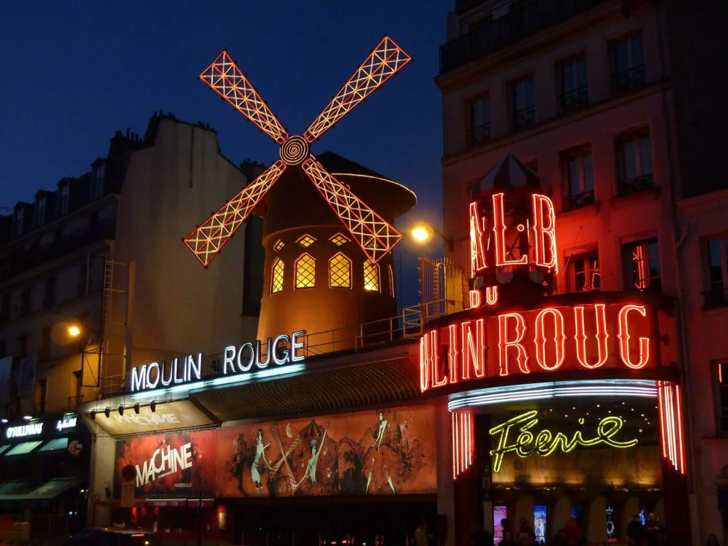 El icónico Moulin Rouge de noche con su famoso molino rojo brillando en Pigalle, París