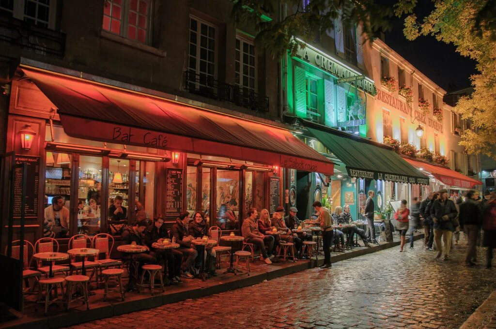 Ambiente nocturno de París con terrazas iluminadas, cafés y restaurantes con comensales disfrutando de la noche parisina